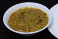  a small white bowl filled with a thick, textured green and yellow chutney or sauce, set against a solid black background.