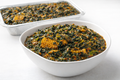Bowl of spinach & collard green vegetable with a pan of the dish in the background on a white surface.