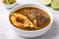Bowl of fish pepper soup with a side of lime wedges on a light surface