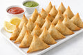 Platter of triangular samosas with dipping sauces and lemon wedges on a white background